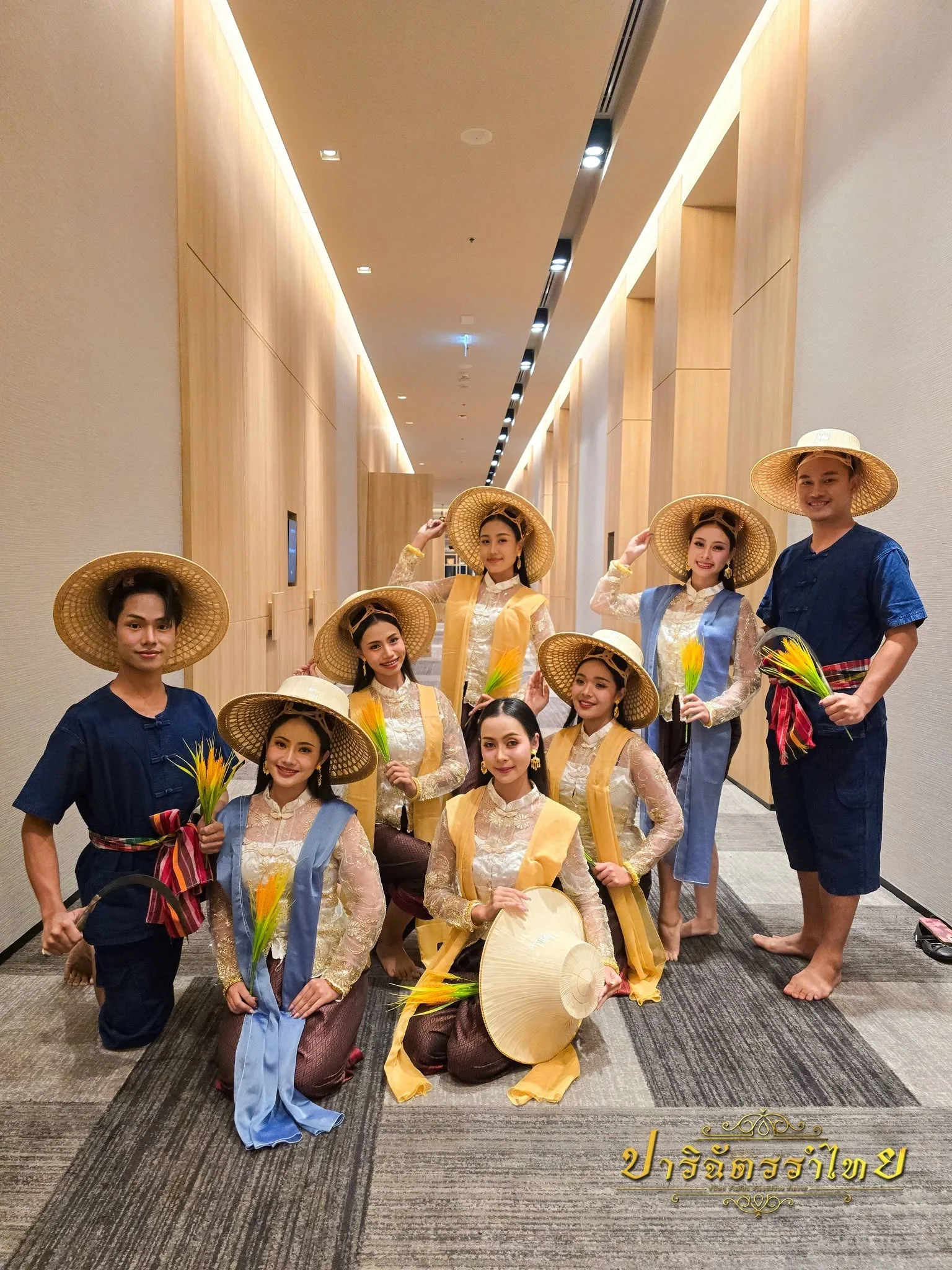คณะผู้แสดงสวมหมวกสานในชุดสีเหลืองและน้ำเงิน